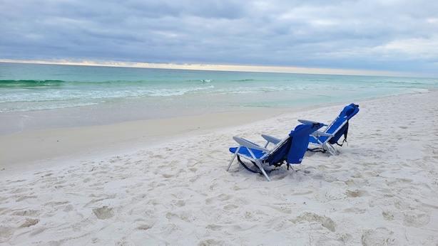 Een strand met twee blauwe ligstoelen en een surfplank.