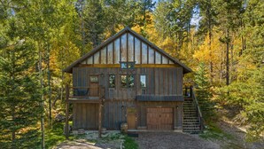 A rustic cabin with a two-story structure, a front porch, and a staircase leading to the upper level. - Whiskey Barrel Lodge (Lead)