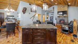 A spacious living area with a large wooden ceiling, a stone fireplace, and a central island with drawers. - Whiskey Barrel Lodge (Lead)
