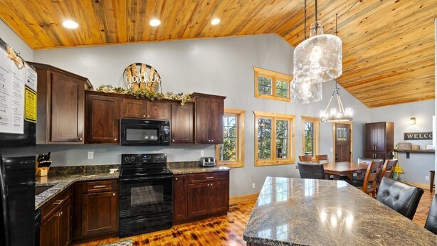 A kitchen with dark wood cabinets, a granite countertop, a black stove, and a large island with a granite top. - Whiskey Barrel Lodge (Lead)
