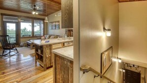 A spacious kitchen with wooden cabinets, a central island, and a dining area with a rocking chair. - Après Powder Haus – Walk to the slopes!  Hot tub, pet friendly and game garage (Lead)