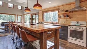 Une cuisine avec un îlot central en bois, des tabourets de bar, une cuisinière et de grandes fenêtres.