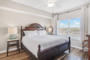 A bedroom with a large bed, two bedside tables, a ceiling fan, and a window with blinds.
