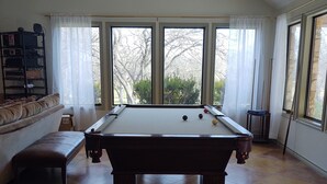 Een pooltafel in een ruimte met grote ramen, een bank en een plank met elektronische apparaten.