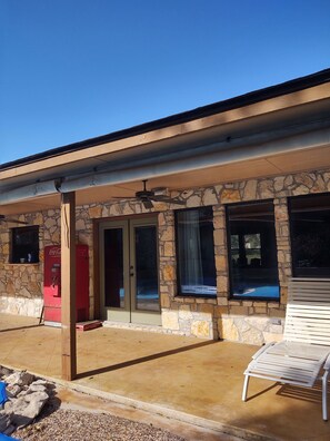 A building with stone walls, a Coca-Cola vending machine, and a patio with a white chair. - Restoration Retreat with Pool and Hot Tub! (Seguin)