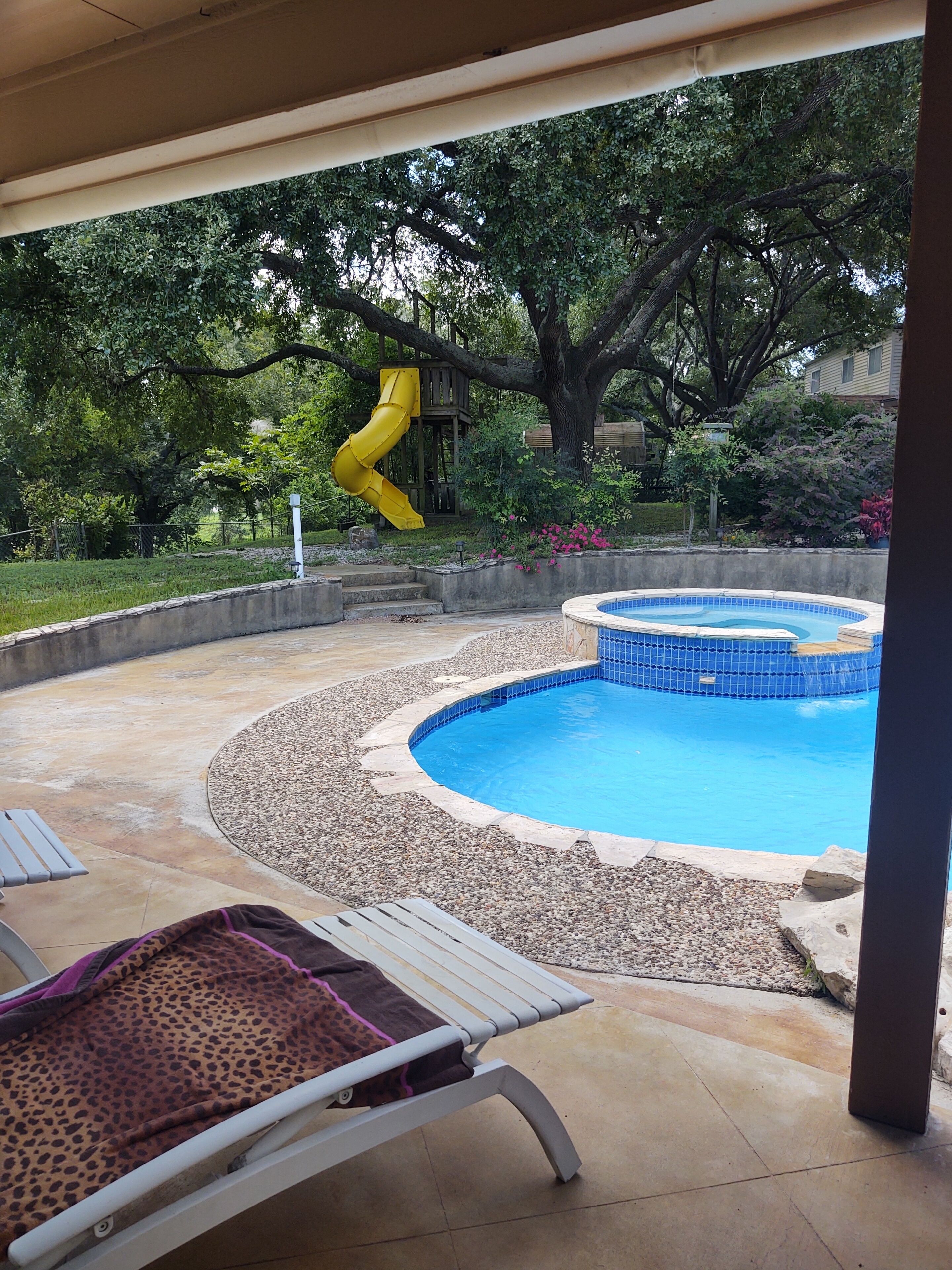 A backyard with a swimming pool, a slide, and a covered patio area.