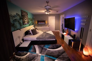 A modern bedroom with a bed, a TV, a heater, and a wall-mounted shelf.