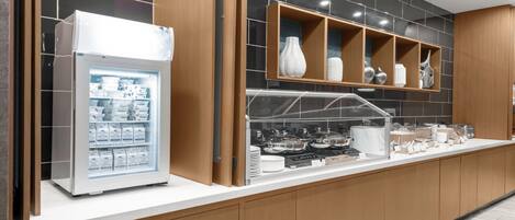 A modern kitchen with a refrigerator, shelves with decorative items, and a buffet counter with food items.