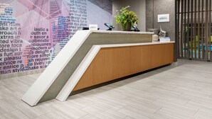 A modern reception desk with a wooden finish, a large wall with text, and a potted plant. - SpringHill Suites by Marriott Raleigh Apex (Apex)