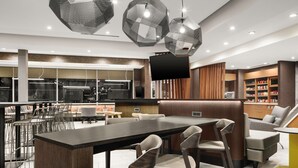 A modern restaurant with a long communal table, bar seating, and a television screen. - SpringHill Suites by Marriott Raleigh Apex (Apex)