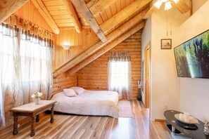 A cozy wooden cabin bedroom with a sloped ceiling, a bed, a bedside table, and a TV mounted on the wall. - Private Cabin · Heated Pool, Sauna & Hot Tub · 2 Acres (Tunkhannock)