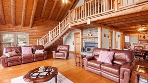 Un interior espacioso de cabaña de troncos con escalera de madera, sofás de cuero, chimenea y comedor.