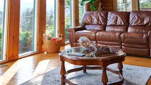 Un salón espacioso con sofá de cuero, una mesa de centro de madera y grandes ventanales que ofrecen vistas al exterior.