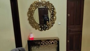 Un pasillo con dos sillones grises, un espejo decorativo y una consola con una lámpara roja.