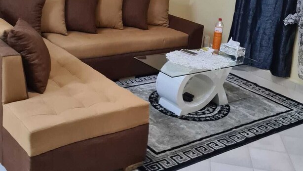 Una sala de estar con un sofá seccional color beige, una mesa de centro de vidrio y un cuadro de una escena boscosa.