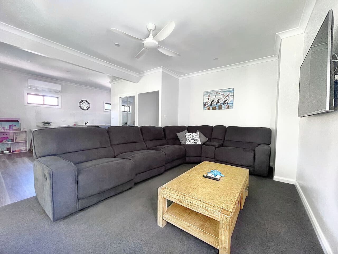 Un salon moderne avec un canapé d’angle gris, une table basse en bois et un ventilateur de plafond.