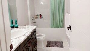 Een badkamer met een witte wastafel, donkerhouten kastjes, een wit toilet en een douche met een groen gordijn.