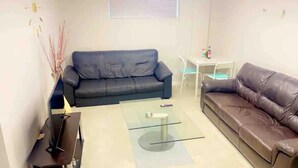 Een woonkamer met een donkerblauwe bank, een bruine leren bank, een glazen salontafel en een kleine witte tafel met een stoel.