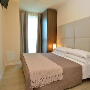 A hotel room with a bed, a nightstand, a wall-mounted TV, and a window with curtains. - SAN Giuliano (Mestre)