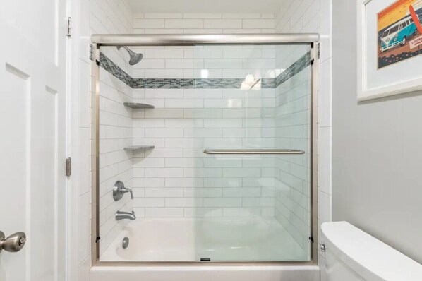 A glass-enclosed shower stall with a bathtub, white tiled walls, and a framed picture on the wall. - Gone Coastal Top Floor, Bay Views, Pool, 120th Street, Quiet Neighborhood (Ocean City)