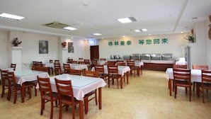 A dining area with multiple tables and chairs, a wall-mounted menu board, and a counter with food display. - Greentree Inn Jinan Tianqiao District Railway Station Square Express Hotel (Jinan)