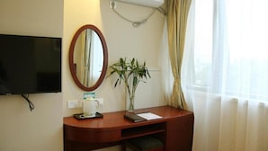 A hotel room with a desk, a television, an air conditioning unit, a mirror, a plant, and a window with curtains. - Greentree Inn Jinan Tianqiao District Railway Station Square Express Hotel (Jinan)