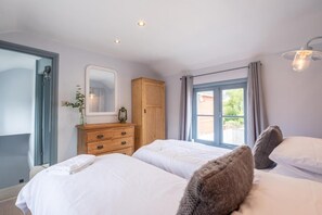 Une chambre avec deux lits, une armoire en bois, un miroir et une fenêtre avec des rideaux.