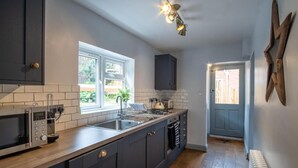 A modern kitchen with dark cabinets, a stainless steel sink, and a built-in microwave. - Sailmaker's Cottage (Lymington)