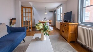 A living room with a sofa, a dining table with chairs, a TV, and a radiator. - Sailmaker's Cottage (Lymington)