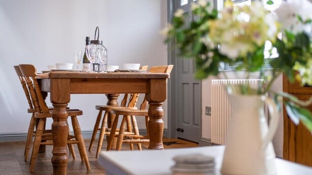 A dining area with a wooden table and chairs, a vase with flowers, and a window with a view. - Sailmaker's Cottage (Lymington)