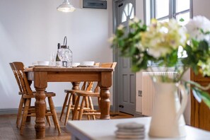 A dining area with a wooden table and chairs, a vase with flowers, and a window with a view. - Sailmaker's Cottage (Lymington)