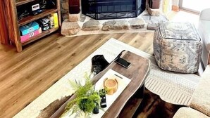 Un salón con chimenea de piedra, un televisor sobre un mueble de madera y un otomano estampado.