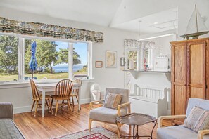 A room with a wooden dining table, chairs, a grey armchair, a small table, and a view of the outdoors.