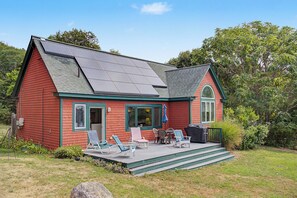 A red house with a green roof, solar panels, a covered patio with chairs, and a barbecue grill.