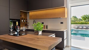 A modern kitchen with dark cabinetry, a wooden countertop, and a view of an outdoor pool. - Luxury Villa Perfecta with Pool (Labin)