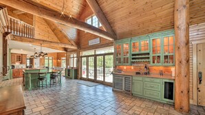 Une cuisine spacieuse avec des meubles de couleur verte, un grand îlot central doté de tabourets, et un plafond en bois.