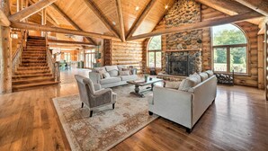 Un intérieur spacieux de chalet en bois, avec un grand salon, une cheminée en pierre et un escalier en bois.