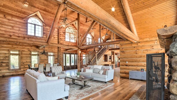 Un intérieur spacieux de chalet en bois, avec un grand salon, un escalier et une cheminée en pierre.