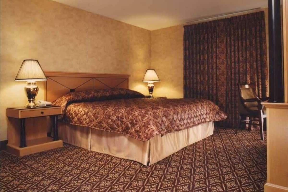 A hotel room with a large bed, two bedside tables with lamps, a chair, and a patterned carpet.