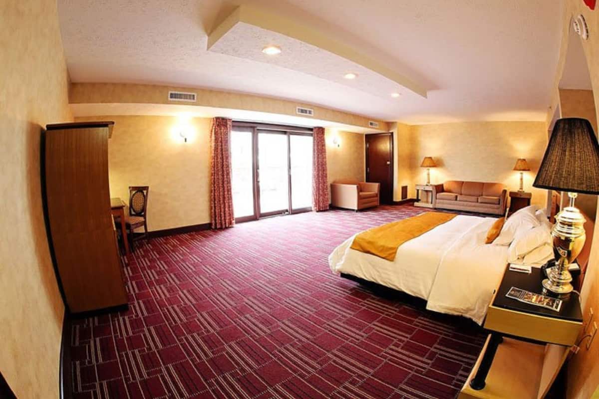 A hotel room with a large bed, a desk with a lamp, a sofa, and a sliding door leading to a balcony.