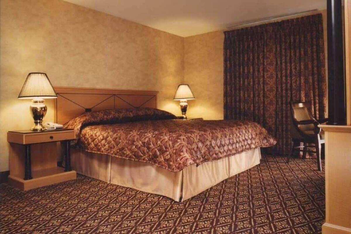 A hotel room with a large bed, two bedside tables with lamps, a chair, and a patterned carpet.