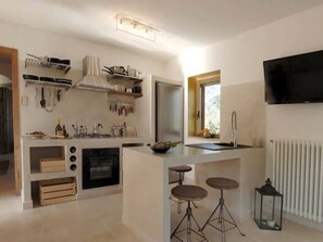 A modern kitchen with a central island, bar stools, a built-in oven, and a TV mounted on the wall.
