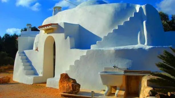 Un edificio blanco y moderno con un diseño arquitectónico único, que presenta una escalera que conduce a una entrada en arco y un pequeño espacio de asientos al aire libre.