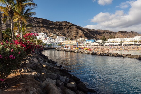 A coastal town with white buildings, a rocky shoreline, and a clear blue sky. - 20 meters from the beach, private parking and AC (Mogán)
