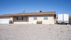 A single-story house with a garage, a small porch, and a utility trailer parked in front. - Mescal Loop Hava-Gataway (Lake Havasu City)