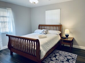 A neatly made bed with a wooden headboard, a bedside lamp, and a patterned rug on a dark wooden floor. - Beautiful Jacksonville Home (Jacksonville)