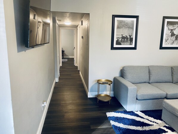 A hallway with a grey sofa and a blue and white rug, leading to a door at the end.