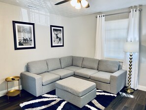 A modern living room with a gray sectional sofa, a matching ottoman, a round gold side table, and a black and white striped rug.