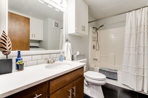 Ein modernes Badezimmer mit Waschbecken, Holz-Waschtisch, Toilette, Dusche mit weißem Vorhang und sichtbarem Lüftungssystem.