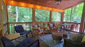 A covered outdoor seating area with wicker furniture, a patterned rug, and large windows overlooking a forested area. - Private Echota home, great resort amenities, 2car garage, near best attractions (Boone)